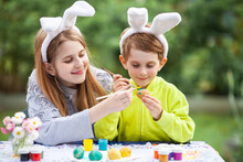 Smiling Children With Rabbit Bunny Ears Painting Eggs For Easter Holiday. Happy Siblings Decorating Eggs For Easter Holiday. Selective Focus.