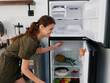© SHOTPRIME STUDIO - A woman opened the refrigerator and looks sadly into it, wondering what to cook, defrosted the refrigerator, freezer repair in the kitchen at home
