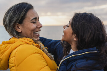 Wall Mural - Latin mother and daughter having tender moment together at sunset during winter time