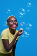 © ADDICTIVE STOCK - Delighted black woman blowing bubbles in studio