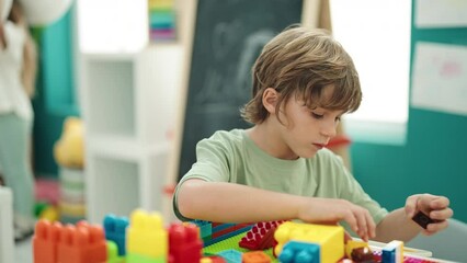 Poster - Adorable caucasian boy playing with construction blocks sitting on table at kindergarten