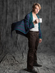 dude after a party in a housecoat with a shaggy head, Holding a mug in his hands and suffering from a hangover, in the studio on a gray background