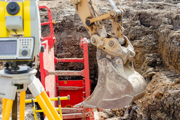 Deep drainage excavation works, with red trench support box installed into the trench and yellow total station next to it