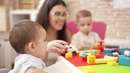 Poster - Teacher with boys playing with construction blocks sitting on table at kindergarten