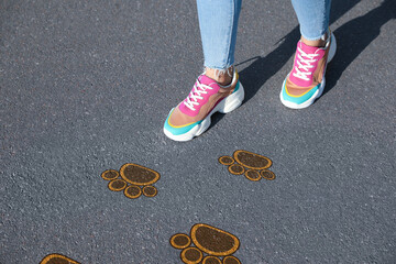 Wall Mural - Planning future. Woman walking on drawn marks on road, closeup. Animal paw prints showing direction of way