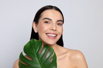 Wall Mural - Woman holding leaf of monstera on light grey background. Spa treatment