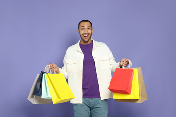 Wall Mural - Happy African American man with shopping bags on purple background