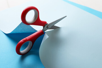 Wall Mural - Red scissors cutting light blue paper on white background, closeup