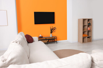 Canvas Print - Stylish sofa and wooden furniture near orange wall in spacious room. Interior design