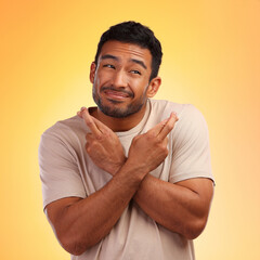 Fingers crossed, man and model with a orange studio background with hand sign for luck. Smile, hope and faith of a person with beard holding hands gesture for wish and optimism feeling hopeful