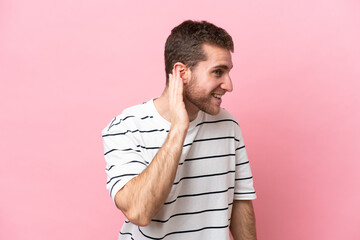 Wall Mural - Young caucasian man isolated on pink background listening to something by putting hand on the ear