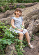 © malyutinaanna - A cute little girl sits on huge tree roots, walks in the fresh air in summer, the child is wearing a summer dress. Summer sunny day. Children's holidays.