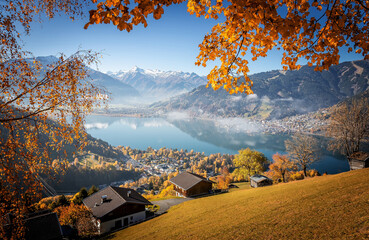 Papier Peint - Colorful misty morning in the Alps mountains. autumn foggy scenery. Amazing nature background. Mountainous autumn landscape. Red folliage on trees and fog in the distant valley. Zell am see lake