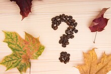 Question Mark. A Question Mark Collected From Roasted Coffee Beans Lies On A Wooden Tabletop. Nearby Are Several Maple Autumn Leaves.