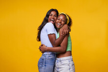 Two Diversity Pretty Positive Girls Toothy Smile Hugging Isolated On Yellow Color Background. Young Lesbian Lovers Couple Embracing And Looking Camera. Friendship And Homosexual Relationship.