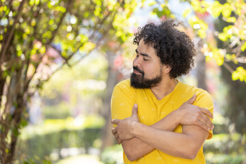 young Mexican man with beard and afro hugging himself, self love concept