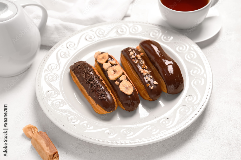 Plate with sweet chocolate eclairs on light background