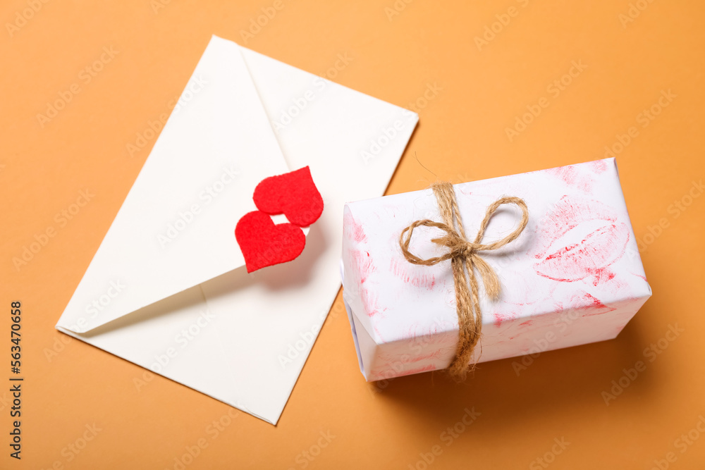 Gift with lipstick kiss marks and envelope on orange background