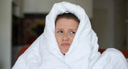 Portrait of young unhappy depressed girl, beautiful lazy lonely woman covering herself in blanket, suffering from depression with sad upset frustrated look at home in living room in early morning