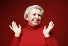 A Cheerful Old Woman In A Red Sweater Laughs And Rejoices. Portrait On A Red Background.