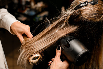 Close-up of hairdo making process. Hairdresser puts female hair with dryer and comb