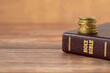 Stack of golden coins on top of holy bible book on a wooden background. Copy space for text. A closeup. Christian tithing, giving, and religious offering concept.