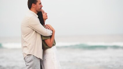 Wall Mural - Young couple in love on the beach summer vacation at sunset. Happy man and woman look at the sea