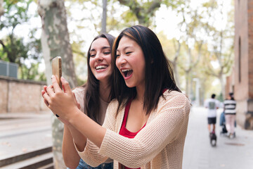 Wall Mural - two young women having fun looking at content on a mobile phone, concept of technology of communication and social media