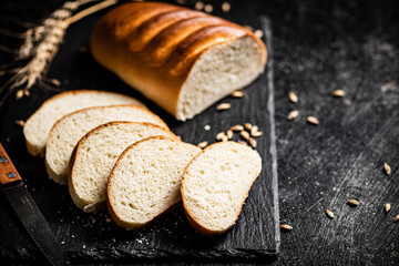 Poster - Sliced wheat bread with a knife on a stone board. 