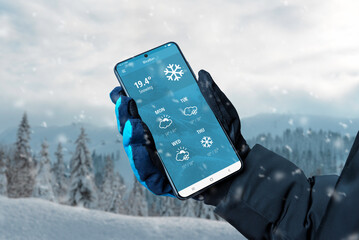 smart phone in hand with glove with weather app on display. winter, snowing time. online service wit