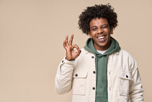Young Happy Hipster African American Guy Student Wearing White Jacket Isolated On Beige Background. Smiling Cool Joyful Ethnic Generation Z Teenager Model Laughing Showing Ok Sign And Winking.
