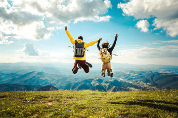 Wall Mural - Hikers with backpack jumping with arms up on top of the mountain