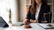 © Parichat - Attractive young lawyer in office Business woman and lawyers discussing contract papers with brass scale on wooden desk in office. Law, legal services, advice, Justice and real estate concept.