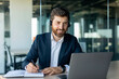 © Prostock-studio - Happy middle aged male manager in headphones looking at laptop and making notes at workplace in office interior