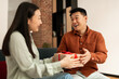 © Prostock-studio - Loving young asian wife giving present to her happy mature husband, sitting on couch at home