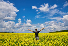 Man Stands In A Yellow Field Rejoicing Raises His Hands To The Sky.