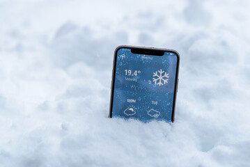 Wall Mural - Phone in the snow with a weather forecast shows the temperature in fahrenheit