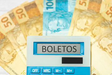 Sticker - A palavra boletos em Português do Brasil escrita em um visor de uma calculadora. Notas do Real Brasileiro no valor de 100 Reais e 50 Reais na composição. Economia brasileira e finanças.