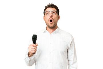 Brazilian man picking up a microphone over isolated chroma key background looking up and with surprised expression