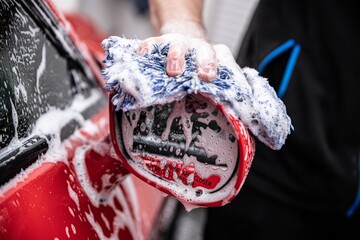 Wall Mural - Employee of a manual car wash carefully washes the car with a sponge and foam