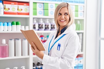 Canvas Print - Young blonde woman pharmacist smiling confident reading notebook at pharmacy