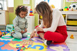 © Krakenimages.com - Teacher and toddler playing with maths puzzle game sitting on floor at kindergarten