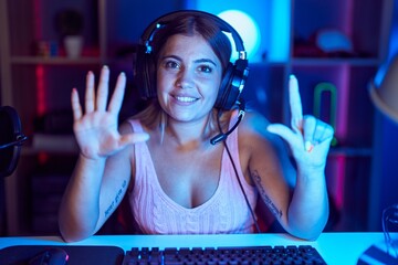 Poster - Young blonde woman playing video games wearing headphones showing and pointing up with fingers number seven while smiling confident and happy.