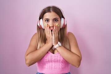 Poster - Young blonde woman listening to music using headphones afraid and shocked, surprise and amazed expression with hands on face