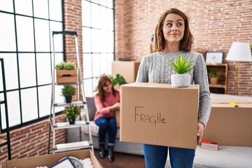 Canvas Print - Mother and daughter moving to a new home holding cardboard box smiling looking to the side and staring away thinking.