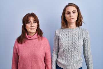 Canvas Print - Mother and daughter standing over blue background relaxed with serious expression on face. simple and natural looking at the camera.