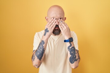 Sticker - Hispanic man with tattoos standing over yellow background rubbing eyes for fatigue and headache, sleepy and tired expression. vision problem