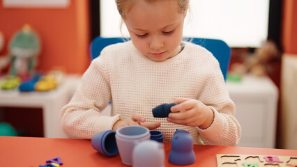 Adorable blonde girl playing with toys sitting on table at kindergarten