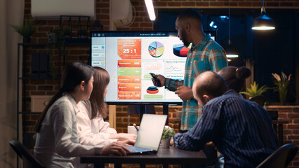 African american employee giving analytics report presentation in business meeting, showing statistics data on digital board screen. Office worker marketing research, strategy planning