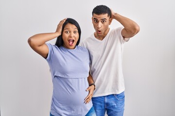 Sticker - Young hispanic couple expecting a baby standing over background crazy and scared with hands on head, afraid and surprised of shock with open mouth